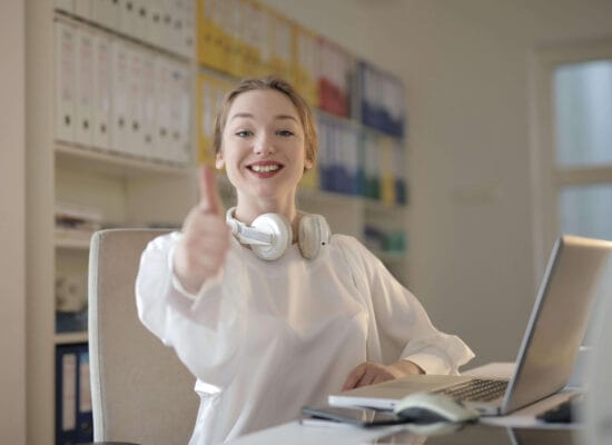 Woman in the office with headphones showing Thumbs Up