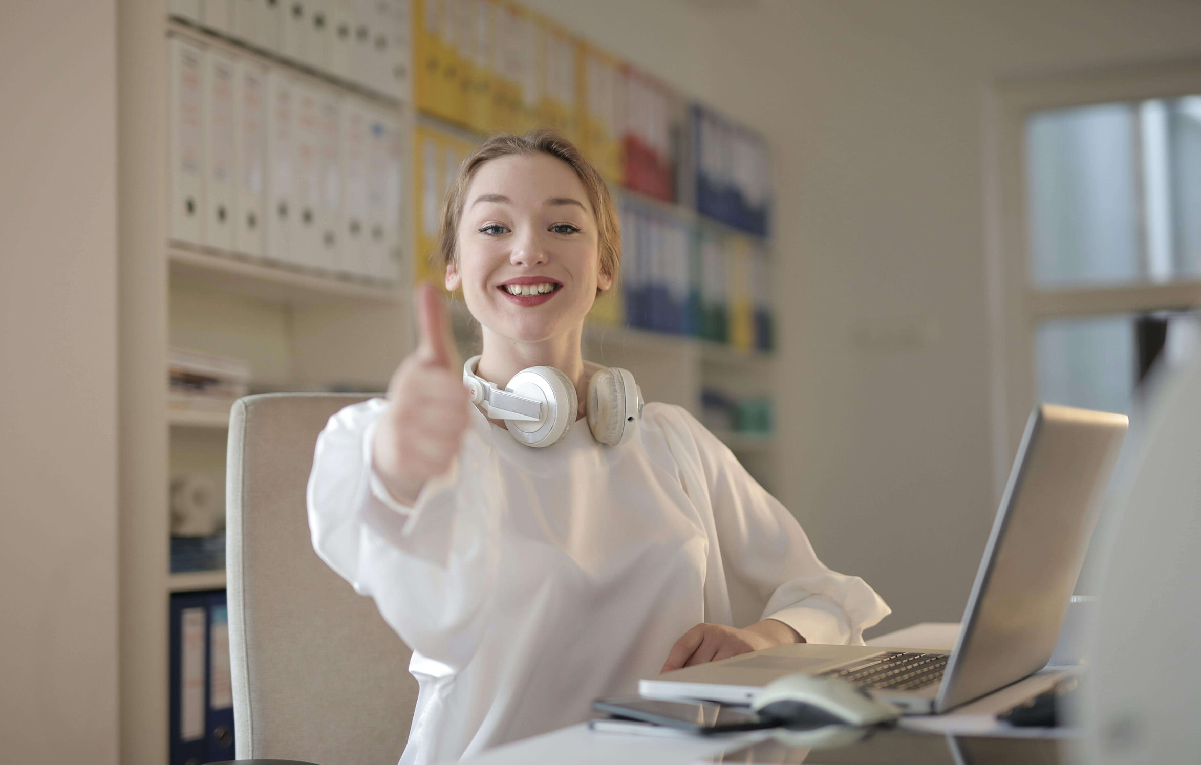 Woman in the office with headphones showing Thumbs Up